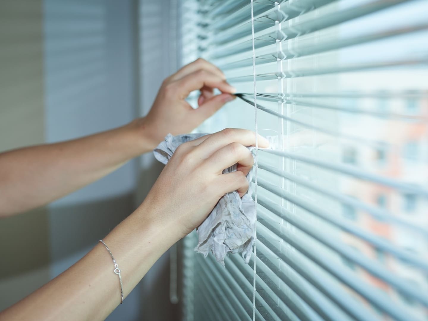 A person cleaning the blinds of their window.