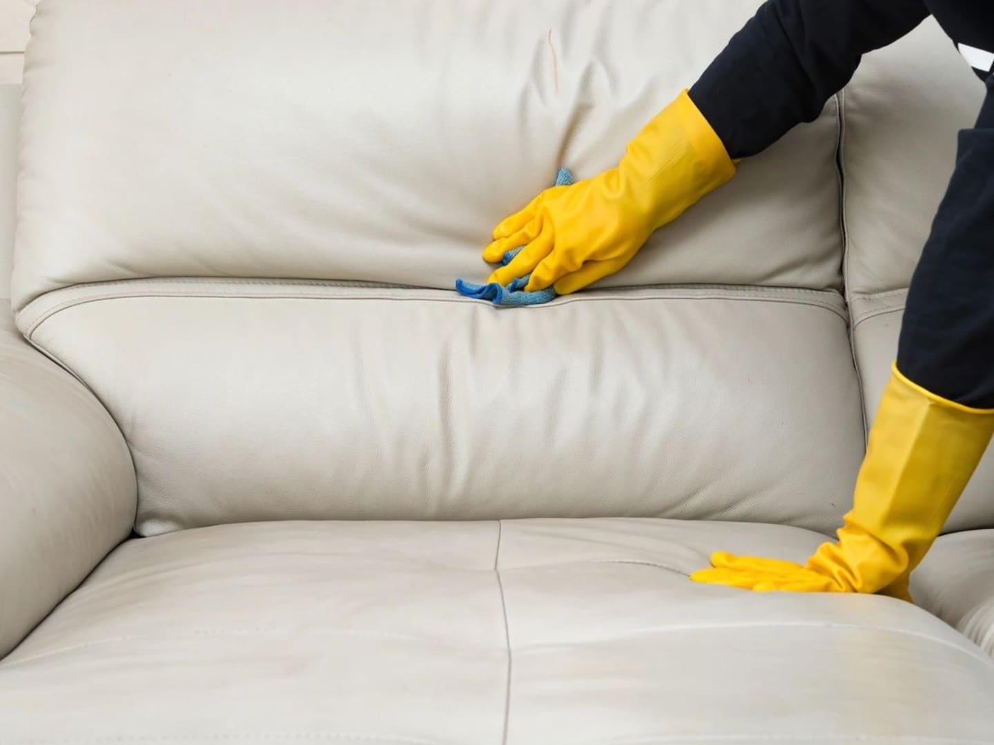 A person in yellow gloves cleaning the leather of a couch.